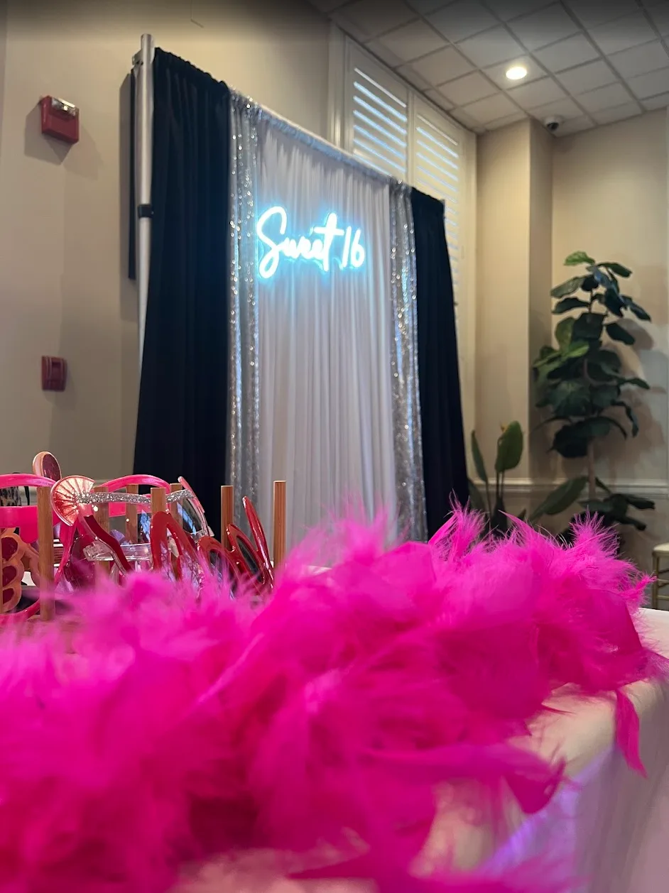 Sweet 16 photo booth with glowing neon sign, sequin backdrop, and pink feather-boa props